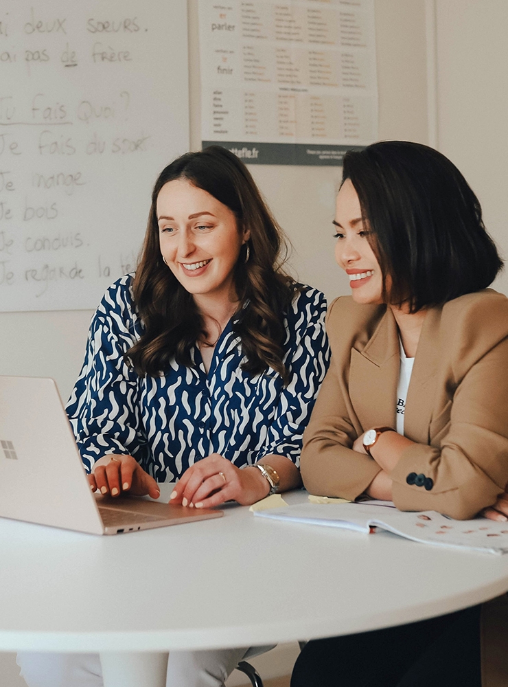 Private French Lessons, Two women smiling while taking online private French lessons together at a table with a laptop and study materials, french private classes, advanced french classes, french night classes
